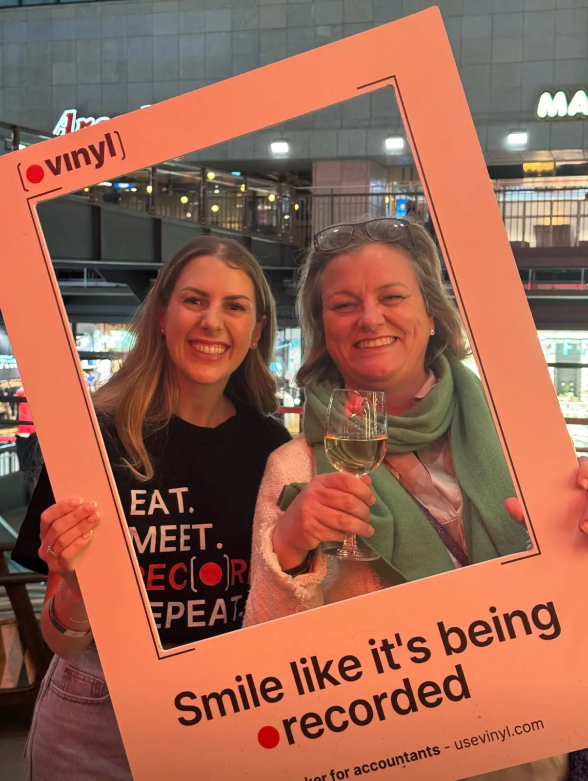 Two attendees posing in a Vinyl-branded photo frame reading 'Smile like it's being recorded' at the launch event